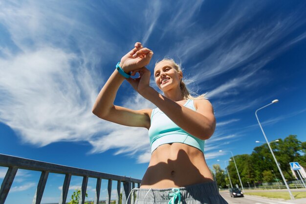 Foto fitness, sport, persone, tecnologia e concetto di stile di vita sano - giovane donna sorridente con orologio per la frequenza cardiaca e auricolari che si esercitano all'aperto