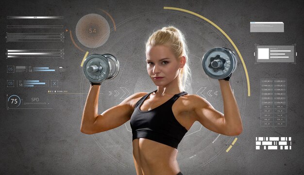 Photo fitness, sport, people and training concept - happy young sporty woman exercising with heavy steel dumbbells over gray concrete background