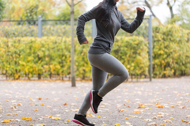 フィットネス、スポーツ、人々、摩耗、健康的なライフスタイルのコンセプト – 秋の公園で走っている若い女性の接写