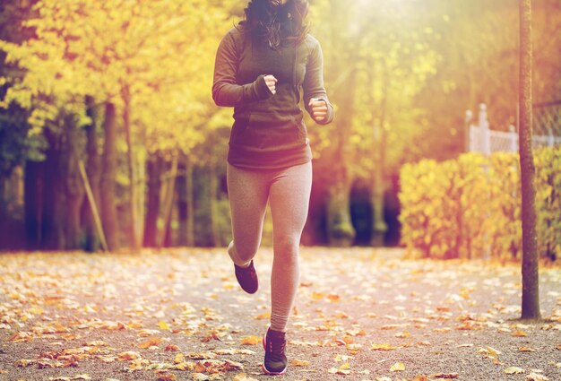 Foto fitness, sport, persone, abbigliamento e concetto di stile di vita sano - primo piano di una giovane donna che corre nel parco autunnale