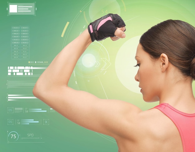 fitness, sport, power, technology and people concept - close up of sporty young woman showing biceps over green background