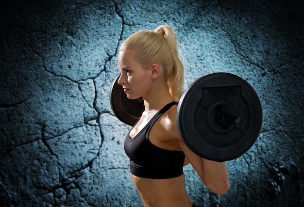 фитнес, спорт, пауэрлифтинг и концепция людей - спортивная женщина тренируется со штангой на фоне бетонной стены