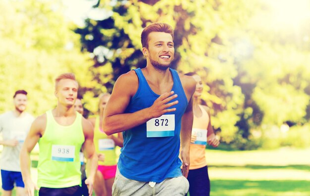 Foto concetto di fitness, sport, razza e stile di vita sano - gruppo di amici adolescenti felici o sportivi che corrono maratona con numeri di badge all'aperto