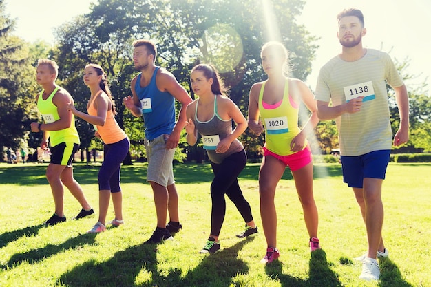 Foto concetto di fitness, sport, razza e stile di vita sano - gruppo di amici adolescenti o sportivi con numeri di badge all'inizio della maratona di corsa all'aperto