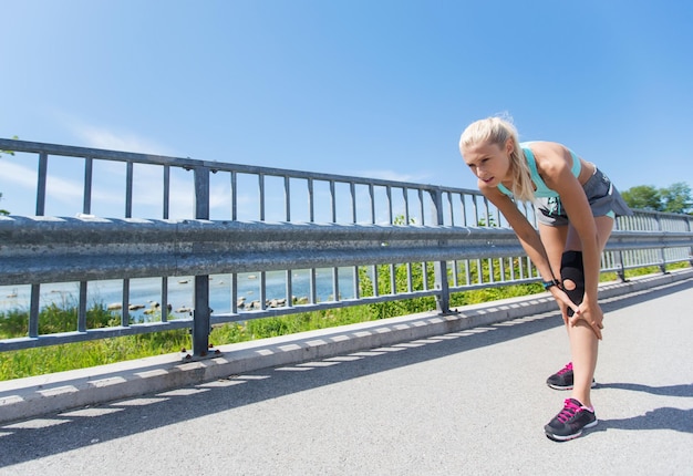 fitness, sport, sporten en gezond levensstijlconcept - jonge vrouw met kniesteun brace gewond been buitenshuis