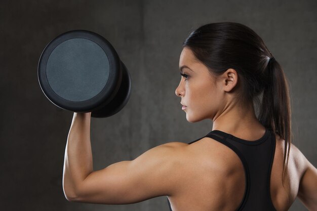 fitness, sport, sporten, training en mensenconcept - jonge vrouw die spieren buigt met halters in de sportschool