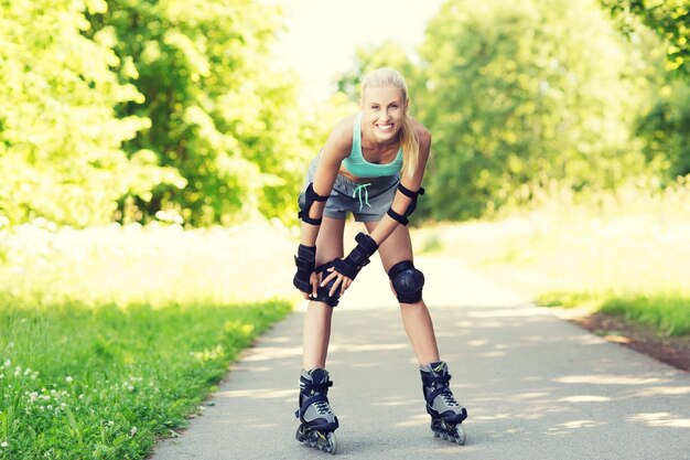 フィットネス、スポーツ、夏、健康的なライフ スタイル コンセプト - ローラー スケートとアウトドアに乗って保護具で幸せな若い女