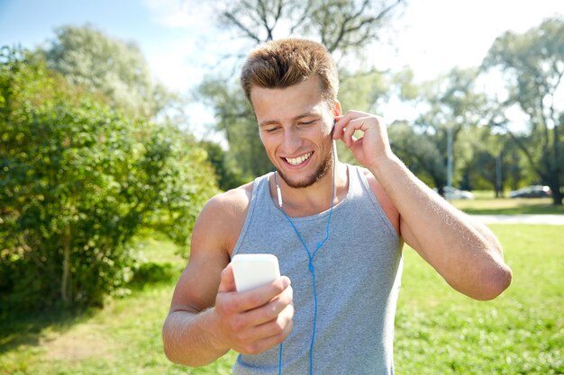 fitness, sport, technologie en lifestyle concept - gelukkige jonge man met smartphone en koptelefoon luisteren naar muziek in het zomerpark