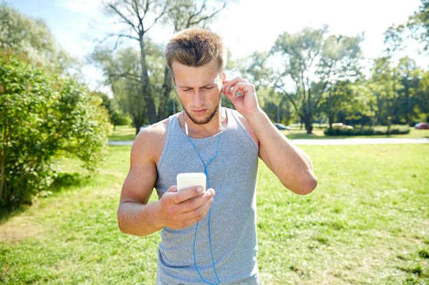 fitness, sport, technologie en lifestyle concept - jonge man met smartphone en koptelefoon luisteren naar muziek in het zomerpark