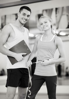 Fitness, sport, allenamento, dieta, palestra e concetto di stile di vita - due persone sorridenti con appunti e metro a nastro in palestra