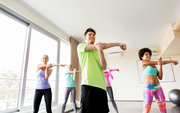 fitness, sport, training and exercising concept - group of smiling people stretching in gym