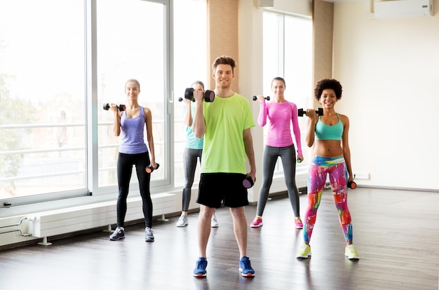 fitness, sport, training and exercising concept - group of smiling people working out with dumbbells flexing muscles in gym