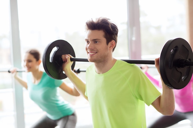 fitness, sport, training, gym and lifestyle concept - group of people exercising with barbell in gym