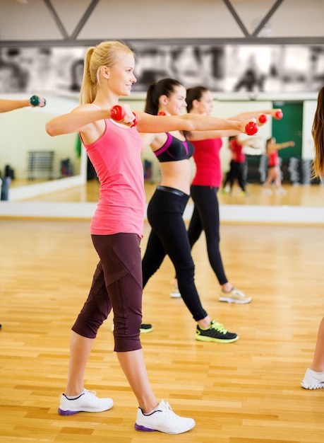 fitness, sport, training, gym and lifestyle concept - group of smiling people working out with dumbbells in the gym