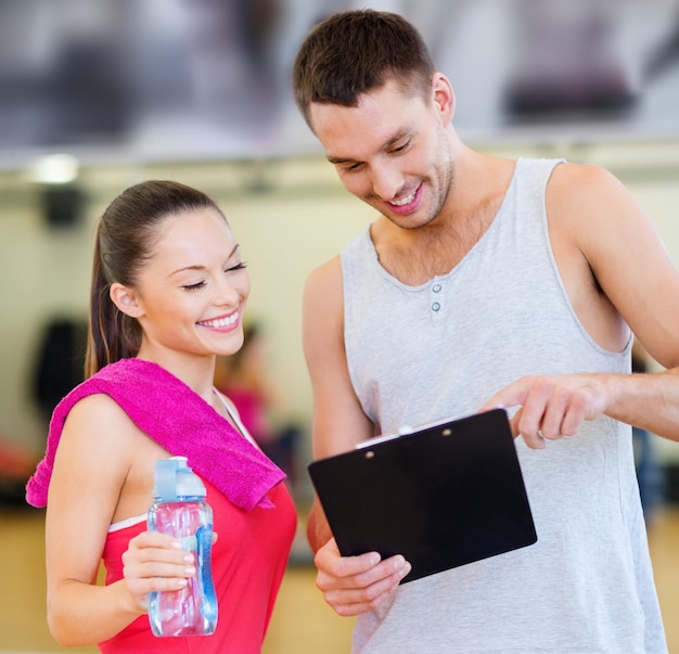 Foto concetto di fitness, sport, allenamento, palestra e stile di vita - allenatore maschio sorridente con appunti e donna con bottiglia d'acqua in palestra