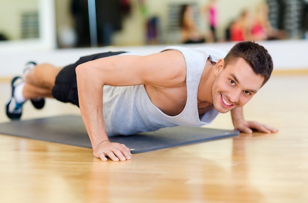 Photo fitness, sport, training, gym and lifestyle concept - smiling man doing push-ups in the gym