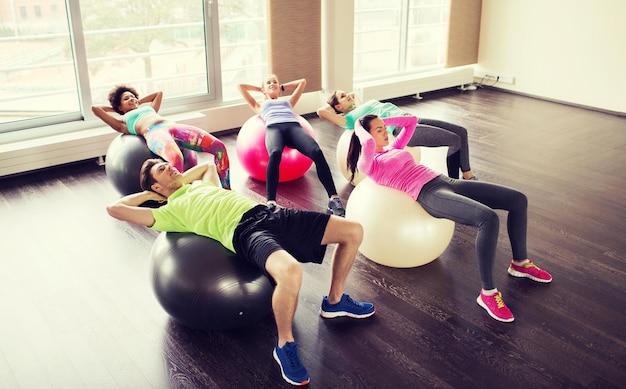 fitness, sport, training and lifestyle concept - group of people flexing abdominal muscles on fitball in gym