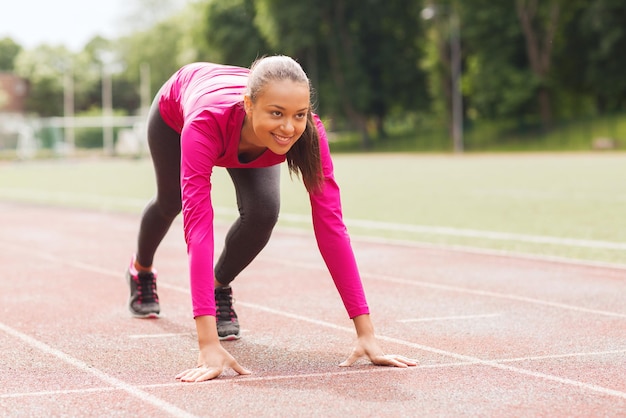 fitness, sport, training and lifestyle concept - smiling african american woman running on track outdoors