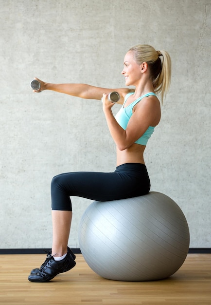 fitness, sport, training and lifestyle concept - smiling woman with dumbbells and exercise ball in gym