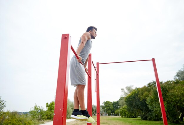 fitness, sport, training and lifestyle concept - young man exercising on horizontal bar outdoors