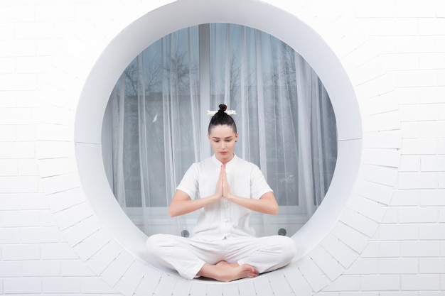 Fitness, sport, training and lifestyle concept - Young woman doing yoga exercise. Portrait of young beautiful girl in white sportswear doing yoga practice.Woman doing stretching exercise