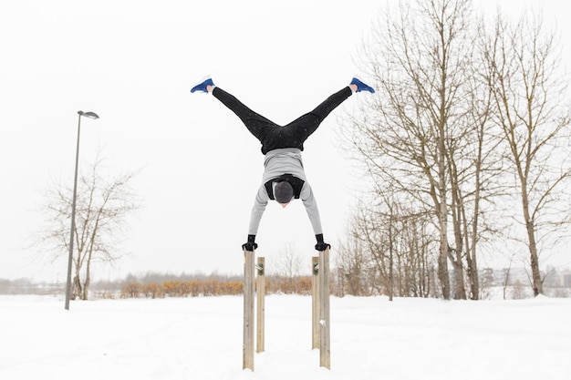 fitness, sport, training, mensen en bewegingsconcept - jonge man op parallelle staven die handstand buiten doen in de winter