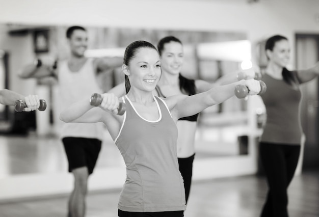 fitness, sport, training, sportschool en lifestyle concept - groep lachende mensen die trainen met halters in de sportschool