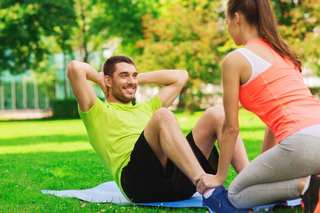 fitness, sport, training, teamwork en lifestyle concept - glimlachende man met persoonlijke trainer die oefeningen op mat buitenshuis doet