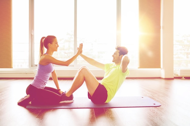 fitness, sport, training, teamwork and people concept - happy woman with personal trainer doing sit ups and high five gesture in gym