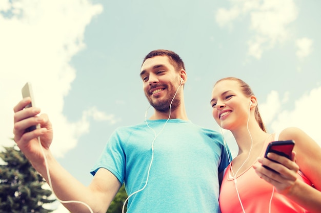 fitness, sport, training, technologie en lifestyle concept - twee lachende mensen met smartphones en koptelefoon buitenshuis