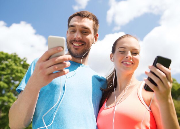 fitness, sport, training, technology and lifestyle concept - two smiling people with smartphones and earphones outdoors