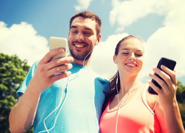 피트니스, 스포츠, 훈련, 기술, 라이프스타일 개념 - 야외에서 스마트폰과 이어폰을 들고 웃고 있는 두 사람
