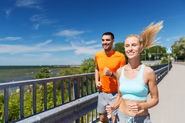 fitness, sport, vriendschap en gezond levensstijlconcept - glimlachend paar dat bij de zomerkust loopt