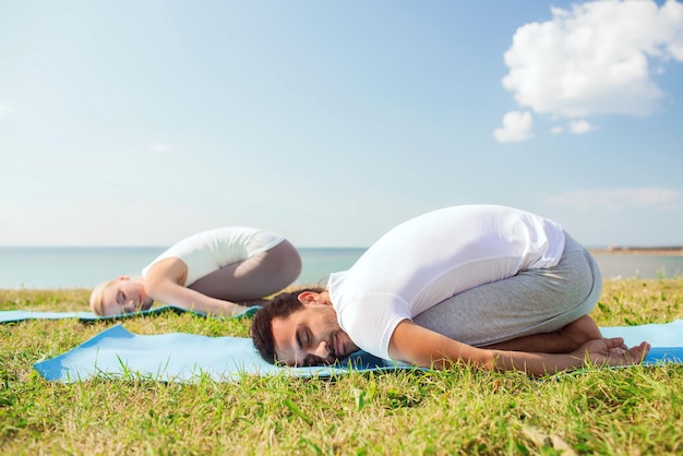 fitness, sport, vriendschap en lifestyle concept - glimlachend paar dat yoga-oefeningen maakt op matten buitenshuis