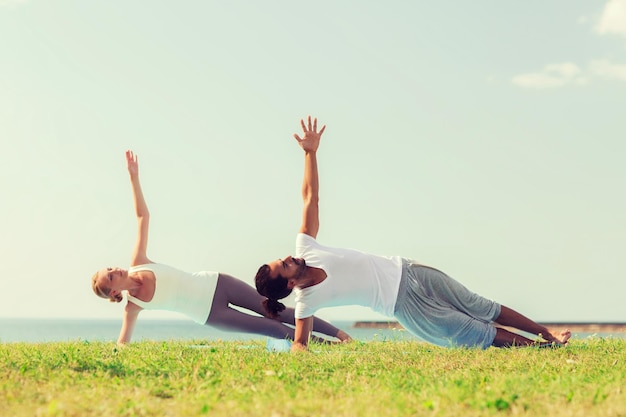 fitness, sport, vriendschap en lifestyle concept - glimlachend paar dat yoga-oefeningen maakt op matten buitenshuis