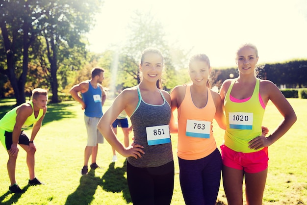 Foto fitness, sport, vriendschap, marathon en gezond levensstijlconcept - gelukkige jonge sportieve vrouwen met racebadgenummers buitenshuis