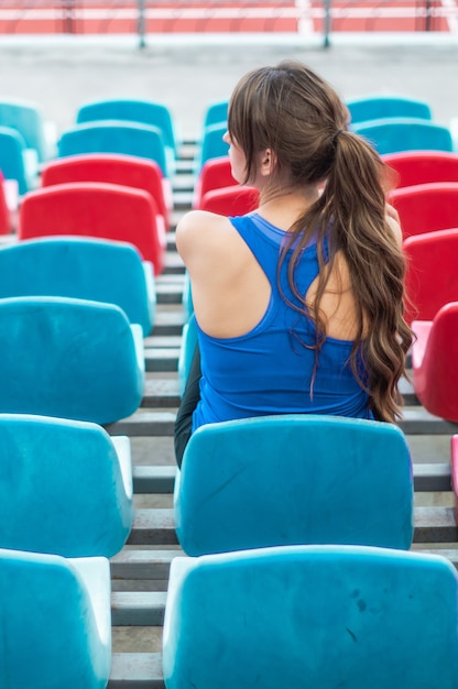 ファッションスポーツウェアのフィットネススポーツ女性は、ランニングスポーツ女性、スタジアムでのフィットネス運動を見て座っています。健康的なライフスタイルのコンセプトです。