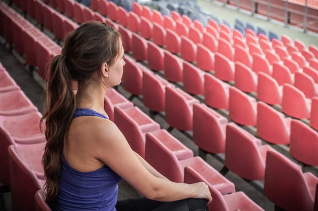 ファッションスポーツウェアのフィットネススポーツ女性は、ランニングスポーツ女性、スタジアムでのフィットネス運動を見て座っています。健康的なライフスタイルのコンセプトです。