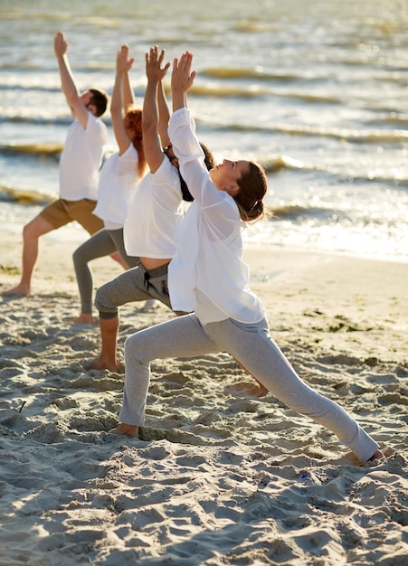Foto fitness, sport, yoga e stile di vita sano concetto - gruppo di persone che fanno un alto lunghe o pose di mezzaluna sulla spiaggia