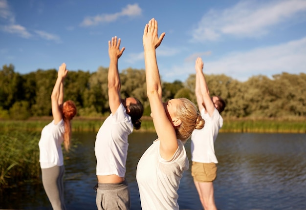 fitness, sport, yoga and healthy lifestyle concept - group of people making upward salute pose on river or lake berth