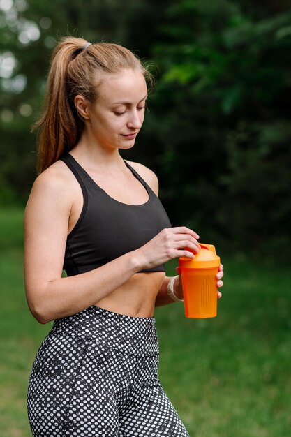 Fitness sportieve vrouw in sportkleding met fles water na trainingen in het park