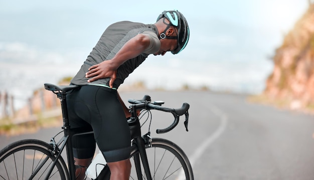 Fitness sports injury and back pain by man cyclist feel uncomfortable while cycling along mountain route Training pain and injured athletic guy suffering from joint muscle and spinal discomfort