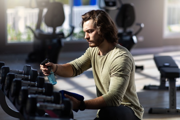 Fitness staff cleaning exercise machines with alcohol sanitizer spray at the gym.