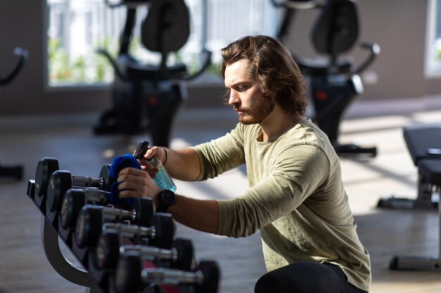 Fitness staff cleaning exercise machines with alcohol sanitizer spray at the gym.