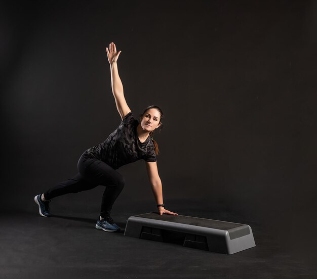 Photo fitness on the step platform on one hand does exercises engaged in sports on a black