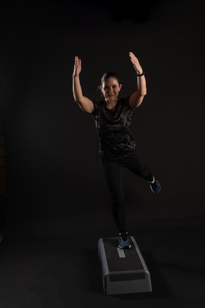 Fitness on a step platform stretching out her arms Going in for sports on a black background