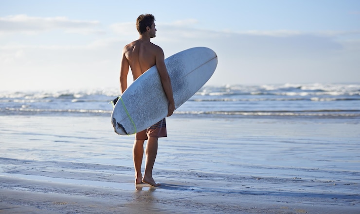 Foto fitness surfen en rug van man op een strand met surfplank voor vrijheid reizen of sporten buiten oceaan training en mannelijke surfer op zee voor zwemmen wellness of avontuur workout of vakantie