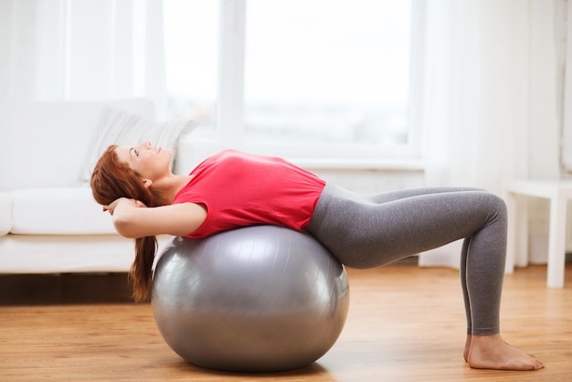fitness-, thuis- en dieetconcept - glimlachend roodharig meisje dat thuis traint met fitnessbal