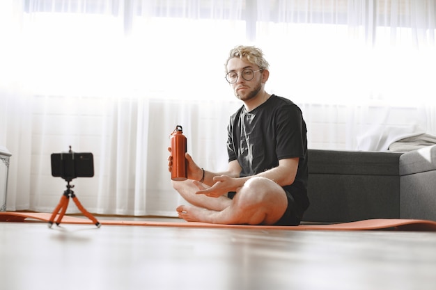 Fitness trainer or video blogger doing stretching. The man is filming himself on smartphone camera at home.