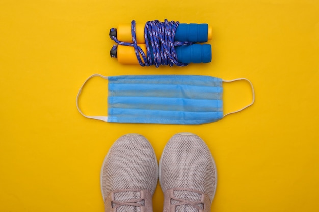 Fitness training during the covid-19 period. Flat lay composition of sneakers, skipping rope, medical mask on yellow background. Healthy lifestyle concept. Top view